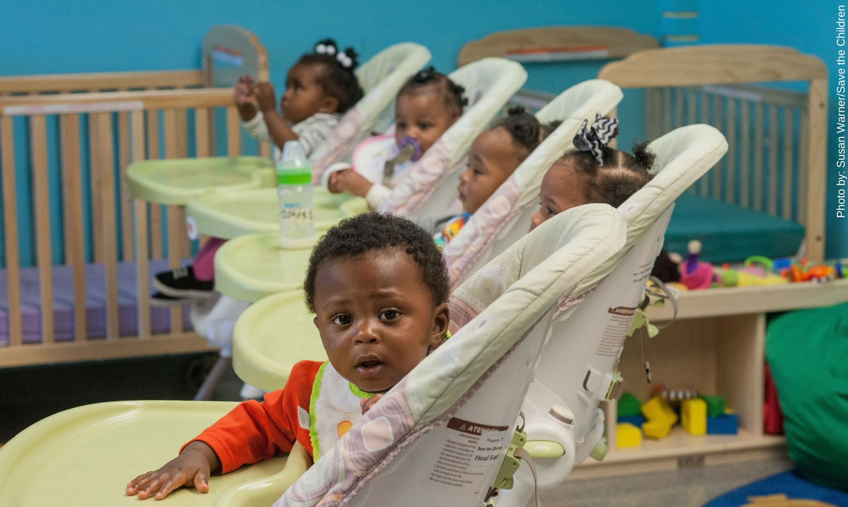 Early Head Start teacher Tywonda Raymond engages her one-year-old students. A curious one-year-old Emery looks on.